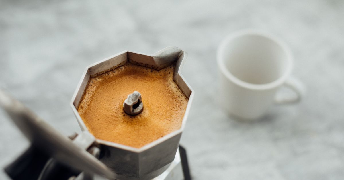 moka pot - filled with coffee, ready to be poured into an empty white cup