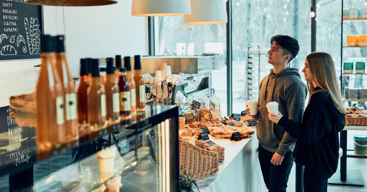 A couple standing in a coffee shop surrounded by pastries and accessories