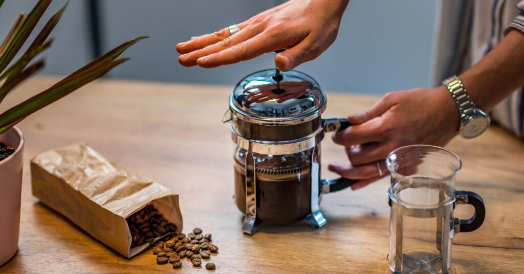 Person plunging a coffee plunger on a table with coffee beans beside it
