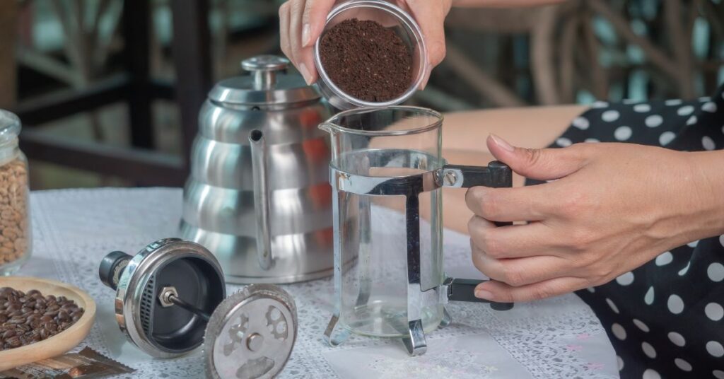 Person pouring ground coffee into a French press
