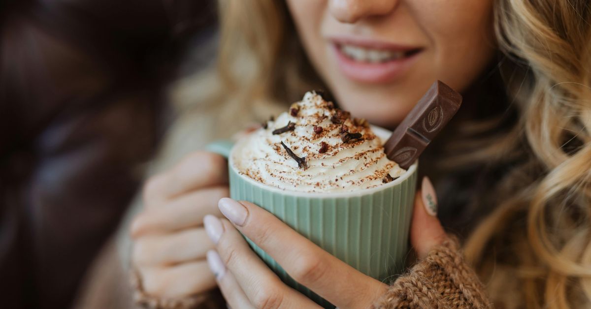 Person holding a hot drinking with cream and chocolate sprinkles on it