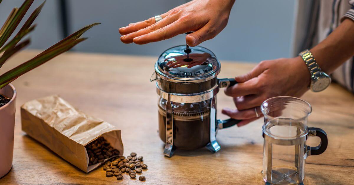 Person pushing down on a french press with a bag of coffee beans on the table