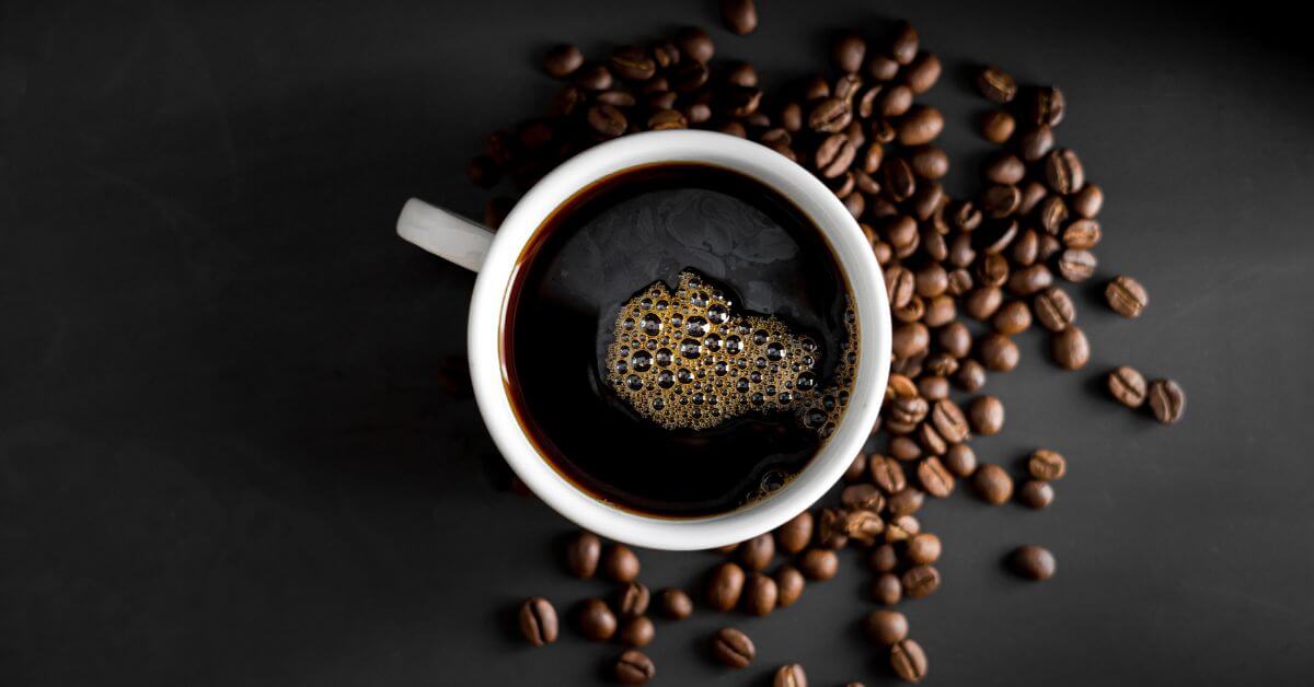 A cup of black coffee on a table with beans around it
