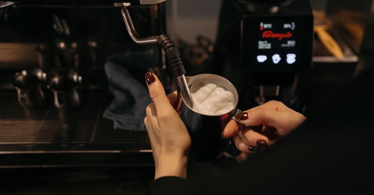 Lady using a steam wand on a coffee machine to froth milk